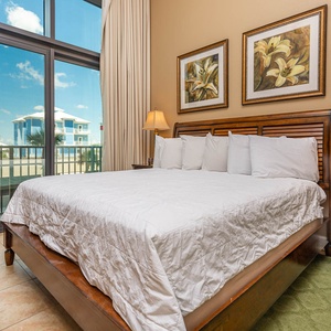 This cozy bedroom features a plush king bed, elegant artwork, and large windows offering a bright view of the surroundings