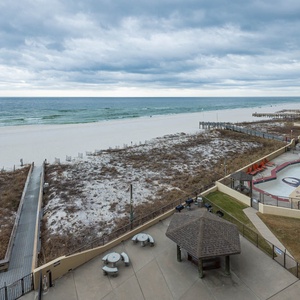 Expansive beachfront view showcasing white sand and gentle waves, with a nearby gazebo and seating area for relaxation