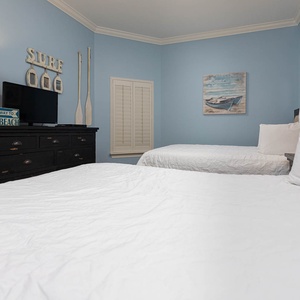 This guest bedroom features two comfortable queen beds, a TV, and beach-themed decor against soft blue walls