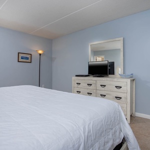 This bedroom features a comfortable bed, a TV, and a view of charming coastal architecture through the window