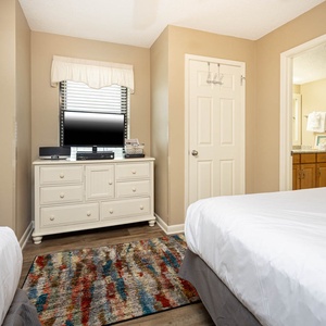 Brightly colored area rug complements two beds and a dresser with a TV, creating a welcoming guest bedroom atmosphere