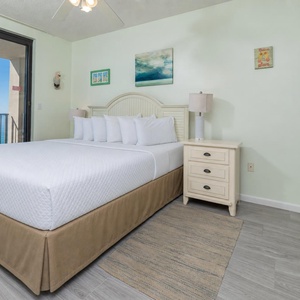 Unwind in the master bedroom featuring a large king bed, soft decor, and access to a balcony with inviting beach views