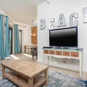 The living area features a cozy blue sofa, a rustic wooden coffee table, twin bunk bed, and a large TV