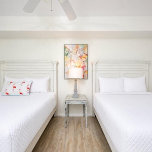 Guest bedroom featuring two queen beds, a colorful artwork, and a rustic nightstand with a lamp
