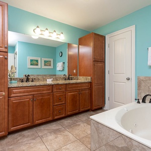 The master bath features elegant cabinetry, a spacious granite countertop, and relaxing jetted tub with a vibrant blue wall