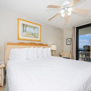 Cozy master bedroom features a large king bed, a wicker headboard, and a TV, all with access to the gulf front balcony