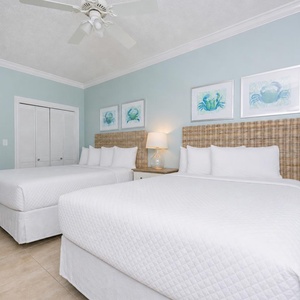 Two queen beds in the guest suite welcome you to unwind under a gentle ceiling fan after a day at the shore