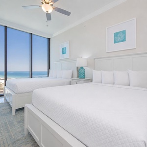 Relax in this guest bedroom with two queen beds and expansive windows showcasing beautiful coastal views