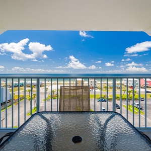 Enjoy a stunning beach view from this balcony, featuring a glass-top table and comfortable seating for relaxation