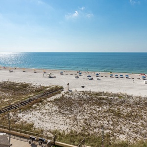 The image showcases a serene beach view with white sand and colorful umbrellas dotting the shoreline under a clear blue sky