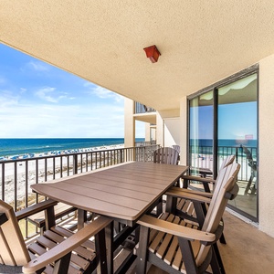 The spacious balcony features a dining table with chairs, offering a captivating view of the beach and turquoise waters