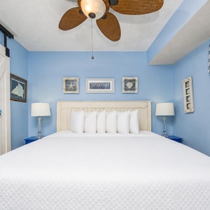 The master bedroom features a cozy king bed with decorative beach-themed accents and a soothing blue color scheme