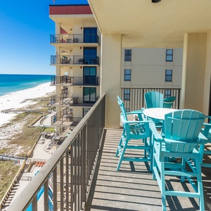 The balcony features turquoise seating and a table, offering a direct view of the white sand beach and sparkling water