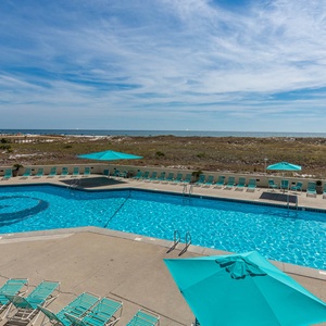 Inviting pool area featuring turquoise umbrellas and lounge chairs, with the beach and Gulf visible in the distance