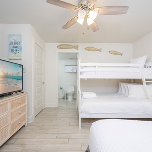 Bright guest room featuring a twin/double bunk bed, a double bed, TV, and light wood flooring, creating a welcoming vibe