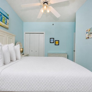 Brightly colored art complements the serene blue walls in this guest bedroom featuring a plush queen bed and tasteful decor