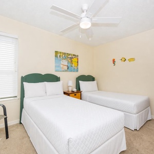 This cheerful guest bedroom features two twin beds, a TV, and beach-themed decor, perfect for a relaxing stay