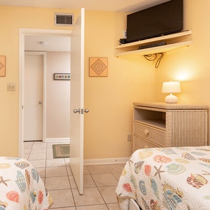 Inviting guest bedroom featuring twin beds, a cozy lamp, and a wall-mounted TV for your entertainment