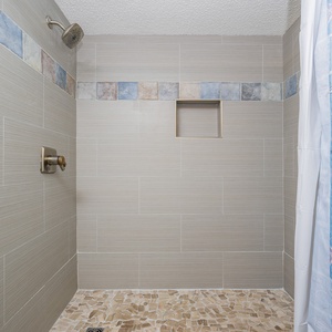 Walk-in shower in the guest bath featuring textured tile walls, rainfall showerhead, and a mosaic floor for a refreshing vibe