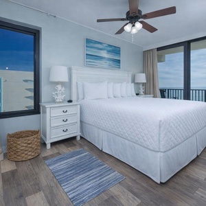 The master bedroom features a king-sized bed, coastal decor, and a stunning beachfront view through large windows