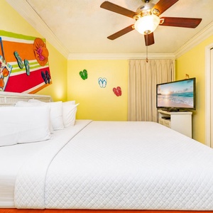 Brightly colored decor complements the spacious bedroom featuring a large king bed, a ceiling fan, and a flat-screen TV