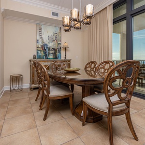 This dining area features elegant wooden chairs around a glass table, with a stunning beachfront view through large windows