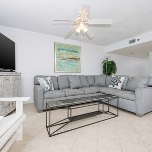 Living area features a large gray sectional sofa, a stylish coffee table, and a wall-mounted TV, creating a welcoming vibe