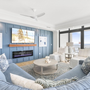 This stunning living area features a plush blue sectional, a mounted TV, and stunning beachfront views through large windows