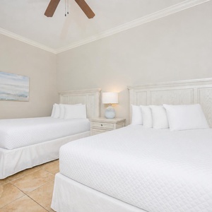 Calming guest bedroom featuring two cozy queen beds, elegant white linens, and a soothing coastal painting