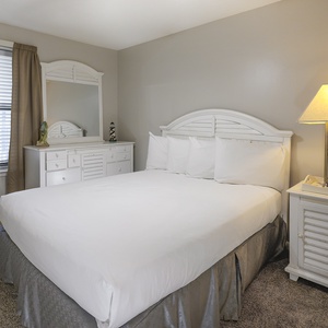 Guest room featuring a queen bed, stylish nightstand, and a dresser with a mirror, complemented by soft curtains