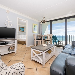The living area features a comfortable sofa, a TV, and a stunning beachfront view from the large glass doors