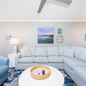 Living area features a light gray sectional sofa with queen sleeper, blue accent chair, and decorative wall art
