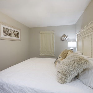 Neutral-toned guest bedroom features a king bed topped with textured pillows, complemented by soft lighting and coastal decor