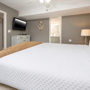 Cozy master bedroom featuring a king bed, flat-screen TV, and a stylish lamp, with a glimpse of the ensuite bathroom