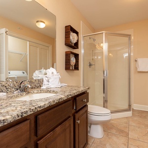 The extra bath features a stylish granite countertop, a glass walk-in shower, and laundry area with a washer and dryer