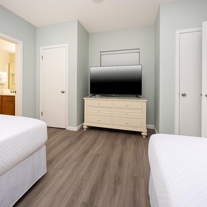 Cozy guest bedroom featuring two double beds, a TV on a white dresser, and an adjoining bathroom for added convenience