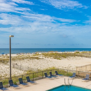 This inviting view showcases a sparkling pool area with lounge chairs and a beautiful beachfront, perfect for relaxation