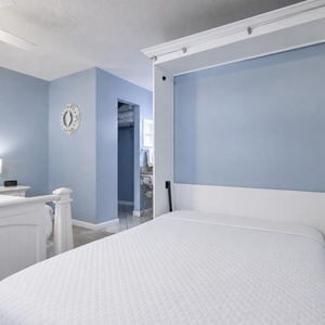 This bedroom features a light blue color scheme, a cozy queen bed, and a convenient fold-out murphy bed