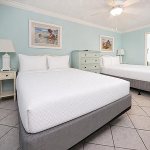 Experience comfort in this guest bedroom with two double beds, light decor, and coastal artwork