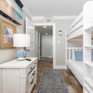 Cozy guest bedroom featuring a stylish queen bunk bed, decorative lamp, and a wall-mounted TV for entertainment