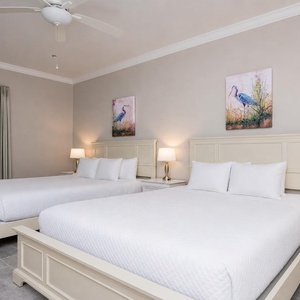 This inviting guest room showcases coastal art adorning two cozy queen beds with fluffy pillows