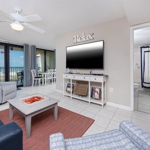 This inviting living area features a large TV, cozy seating, and a beautiful view of the beach through expansive windows
