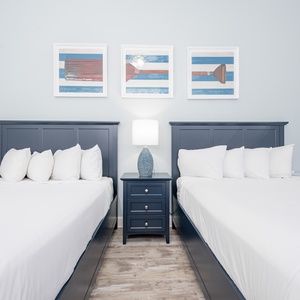 Stylish guest bedroom featuring two cozy queen beds, stylish decor, and a charming bedside lamp