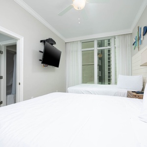 Comfortable guest bedroom featuring two queen beds, a TV, and large windows that let in natural light