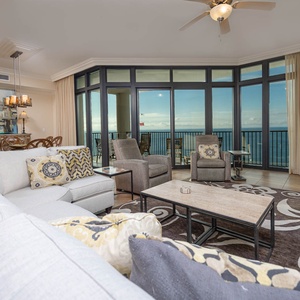The living area features a plush sectional sofa, a stylish coffee table, and beach views through large balcony windows