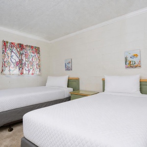The bright bedroom features two twin beds, colorful curtains, and cheerful fish artwork for a fun atmosphere