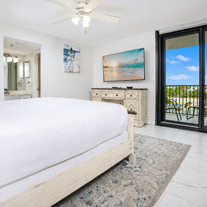 Bright master suite featuring a plush king bed, a large TV, and a sliding door leading to a balcony with views of the area