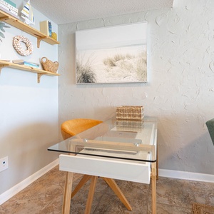 This cozy workspace features a glass desk, colorful chair, and beach-themed decor, perfect for enjoying complimentary WiFi
