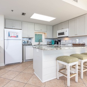 The kitchen features a breakfast bar with green stools, light cabinetry, and a colorful backsplash for a cheerful vibe