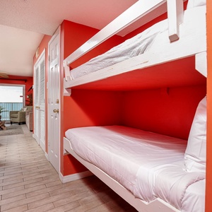 This cozy nook features built-in bunk beds against vibrant red walls, leading to a relaxing view of the beachfront